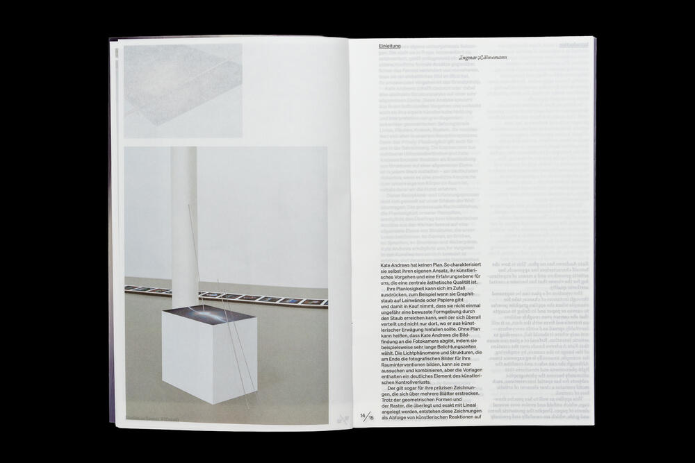 An open exhibition catalog spread showing a white minimalist sculptural object photographed in an institutional gallery space on the left page, with dense text columns on the right page discussing the work and its context.