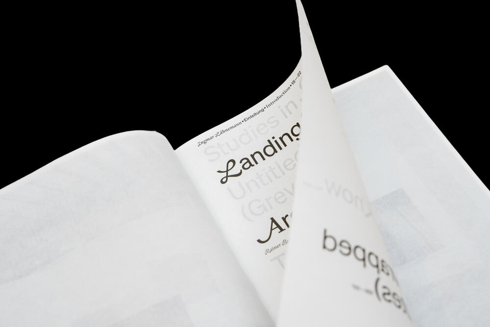 Open pages of a printed exhibition catalog titled "Landing" with visible text fragments and typography on white paper against a black background.