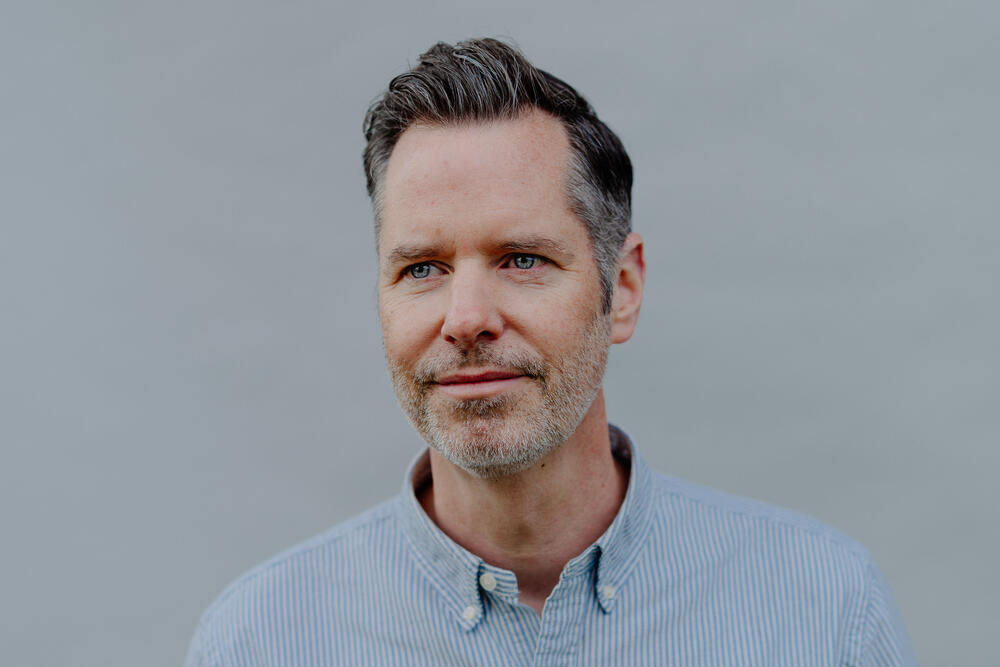 Christian Dürr, a middle-aged man with dark hair and facial stubble, wears a light blue button-up shirt against a neutral gray background. He has a subtle smile and is facing the camera directly in this professional headshot.